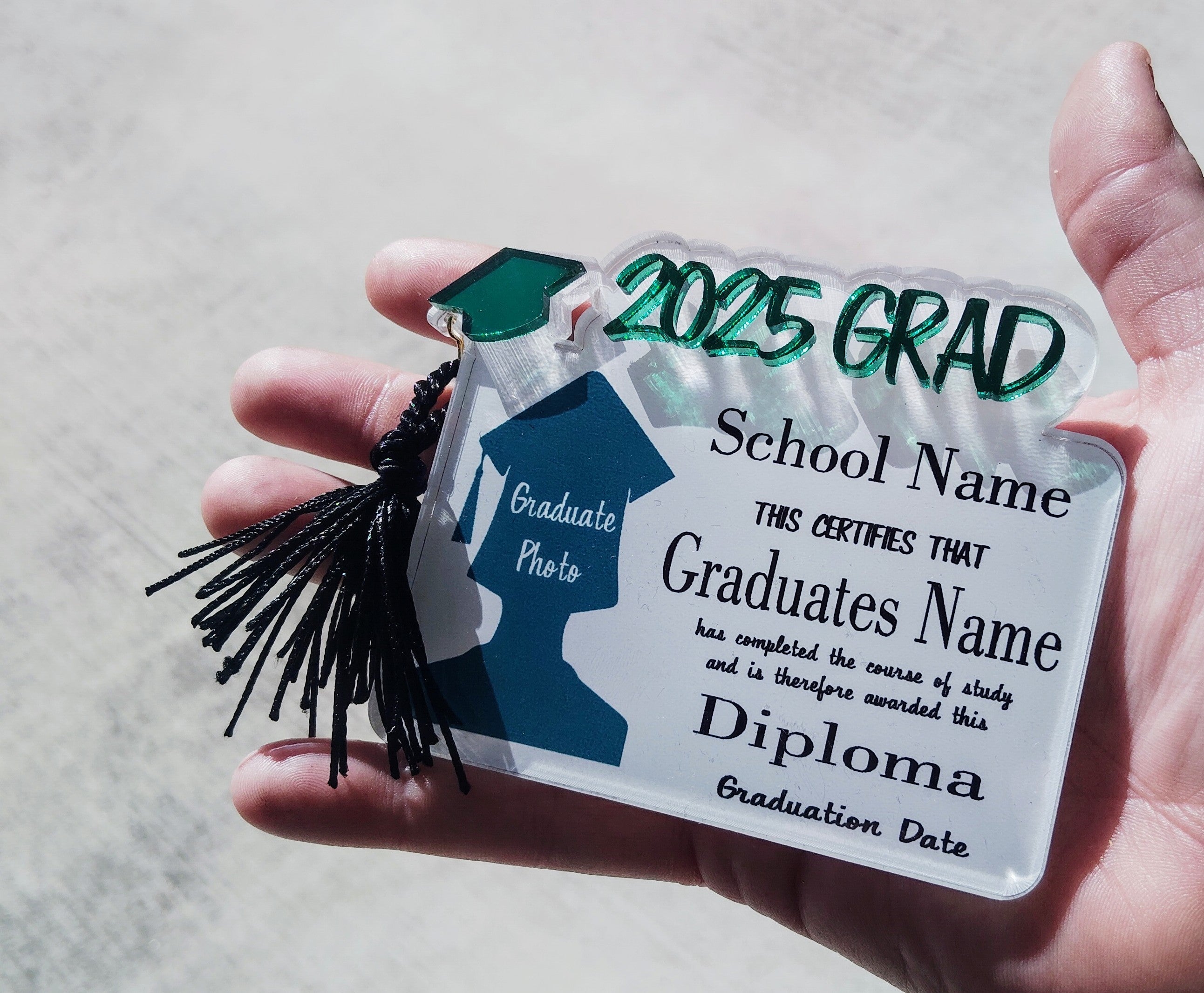 Graduation-themed decorative card with a tassel held in a hand against a neutral background